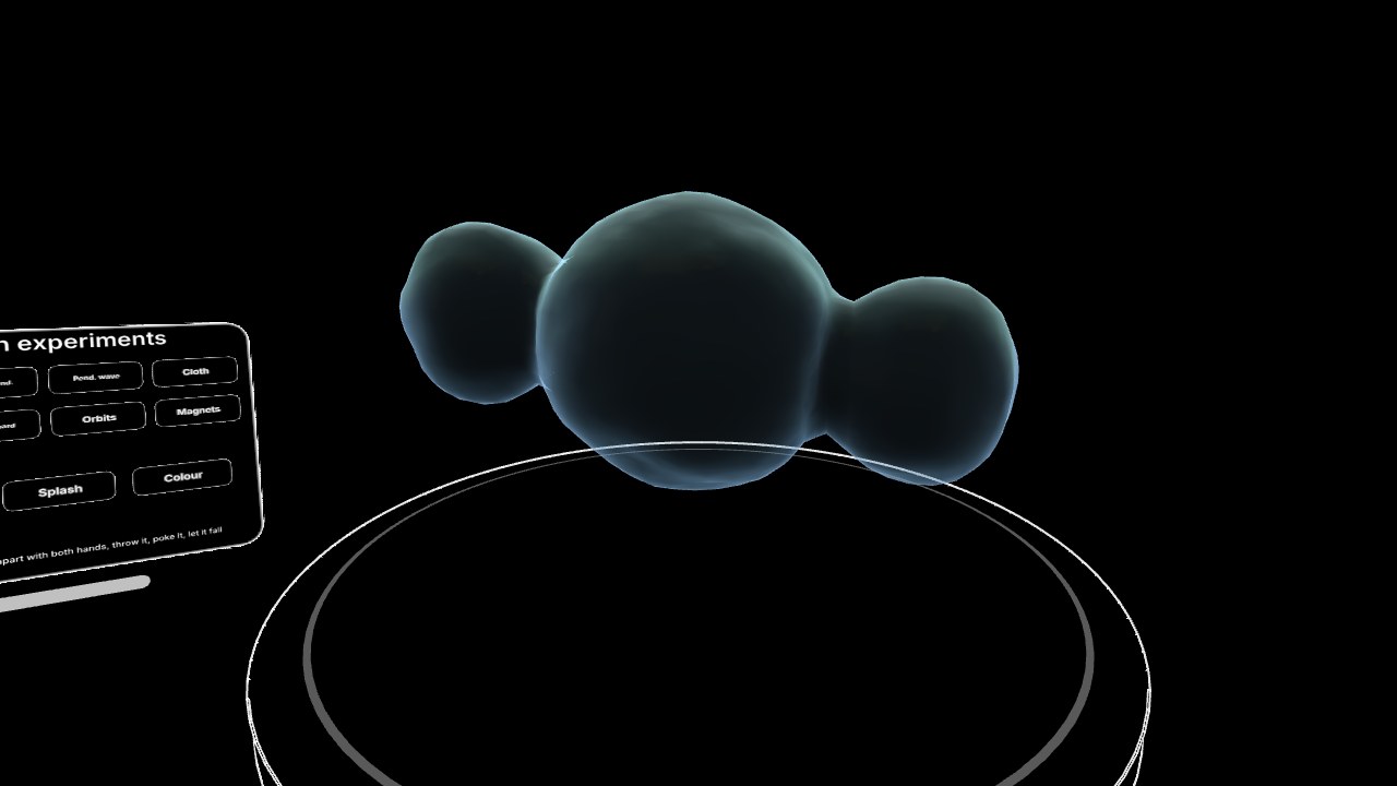 Physics Cabinet: a ball of water pulled apart by two hands into three lobes, floating over the plate.